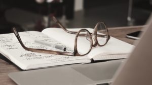Óculos e caneta sobre caderno com anotações