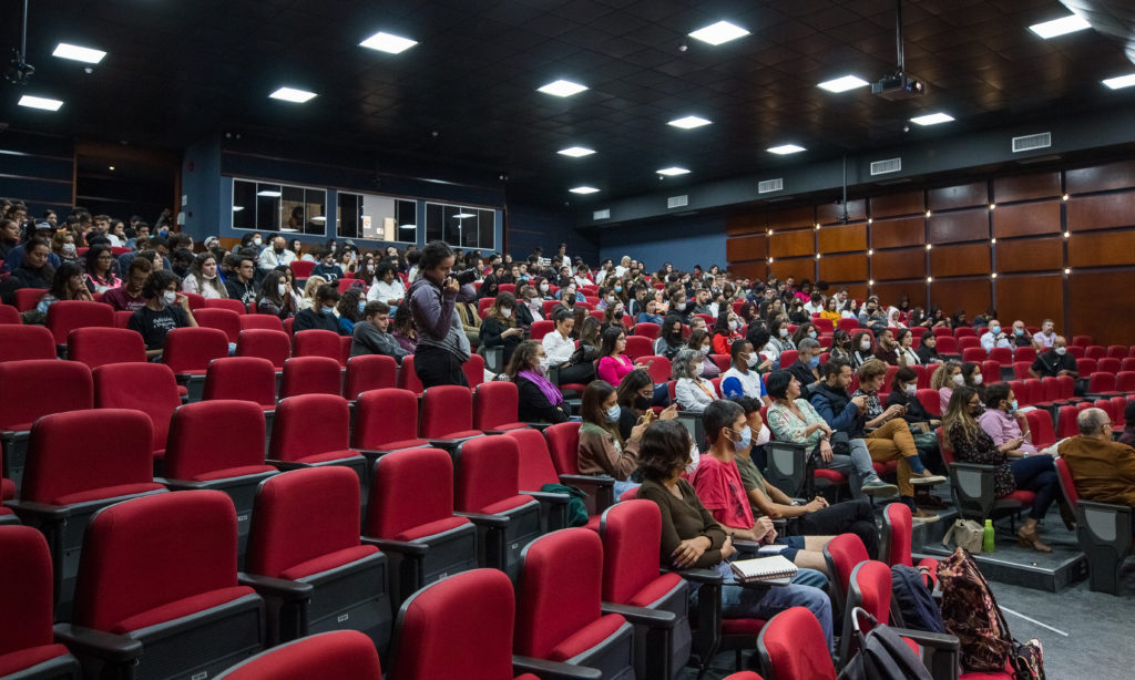 Auditório do prédio 30 com as cadeiras mais próximas vazias e laterais e fundo cheio.